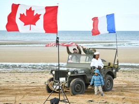 A woman and young child stand with a vintage Willys Jeep at a D-Day 75th Anniversary event on Juno beach on June 6, 2019 in Courseulles-sur-Mer, France.