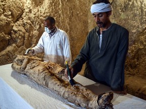 Egyptian archaeological technicians restore a mummy wrapped in linen.