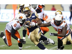 Winnipeg Blue Bombers running back Cameron Marshall (c) breaks a block by BC Lions defensive back T.J. Lee (l) and defensive tackle Jabar Westerman  during CFL football in Winnipeg, Man. Thursday July 30, 2015. Brian Donogh/Winnipeg Sun/Postmedia Network