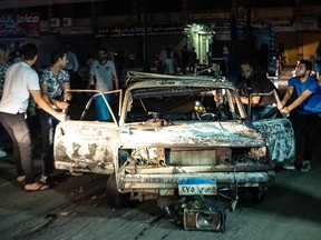 A picture taken early morning on Aug. 5, 2019, shows people surrounding a burned car after an accident that caused an explosion in downtown Cairo.