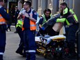 A woman is carried by paramedics, as police officers investigate a scene following reports of a stabbing in Sydney, Australia, on Tuesday, Aug. 13, 2019.