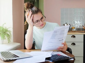 Indoor shot of young European Caucasian girl looking at financial documents at home with deeply bored face looking sick and tired of her economic problems, trying to check counts and all details