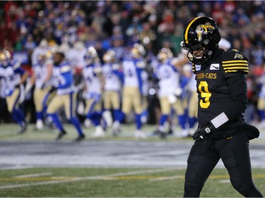 A dejected Hamilton Tiger-Cats quarterback Dane Evans walks off the field as the Winnipeg Blue Bombers celebrate in the background.