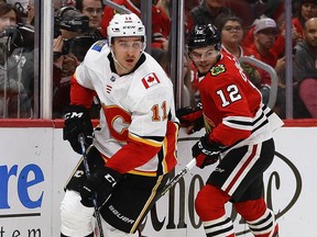 CHICAGO, ILLINOIS - DECEMBER 02: Mikael Backlund #11 of the Calgary Flames looks to pass in front of Alex DeBrincat #12 of the Chicago Blackhawks at the United Center on December 02, 2018 in Chicago, Illinois. The Flames defeated the Blackhawks 3-2. (Photo by Jonathan Daniel/Getty Images)