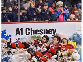 Calgary Hitmen Mark Kastelic, Dakota Krebs and Riley Stotts lie on a pile of stuffies during the Teddy Bear Toss game against the Red Deer Rebels at Scotiabank Saddledome on Sunday. Photo by Azin Ghaffari/Postmedia.