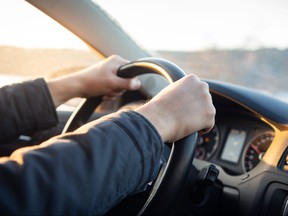 Driver's hand on steering wheel of car in cabin.