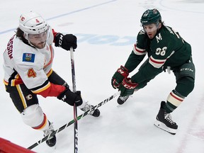 ST PAUL, MINNESOTA - JANUARY 05: Rasmus Andersson #4 of the Calgary Flames and Ryan Hartman #38 of the Minnesota Wild go after the puck during the second period during the game at Xcel Energy Center on January 5, 2020 in St Paul, Minnesota. (Photo by Hannah Foslien/Getty Images)