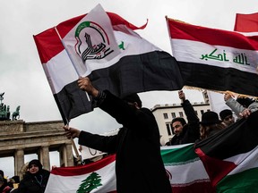 Protesters wave flags of Iraq and a smaller flag with the insignia of the Popular Mobilization Forces (PMF), also known as the People's Mobilization Committee (PMC) and the Popular Mobilization Units (PMU), during a demonstration in front of the U.S. embassy in Berlin on Jan. 4, 2020. (PAUL ZINKEN/dpa/AFP via Getty Images)
