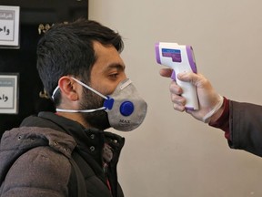 An Iranian man checks the temperature of a person entering an office building in Tehran on March 4, 2020.