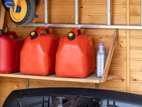 Garage corner with three red plastic fuel cans , staircase and snow plough for atv with wooden wall on background. Petrol gas containers reserves storage at vehicle home garage.