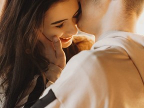 Beautiful close up portrait of an caucasian young couple embracing against light, while boy is kissing his girlfriend cheek which is smiling.