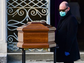 A man wearing a face mask stands by the coffin of his mother during a funeral service in the closed cemetery of Seriate, near Bergamo, Italy, Friday, March 20, 2020.