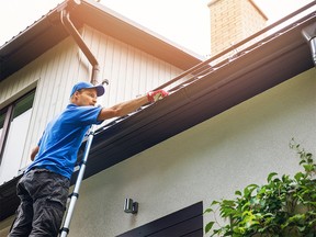 man on ladder cleaning house gutter from leaves and dirt