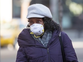 A woman wears a face mask while walking in downtown Calgary on Thursday, March 12, 2020. Flights around the world are being cancelled and more office workers are being asked to work from home to help slow the spread of COVID-19.