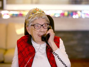 Gladys de Vries talks on the phone with family as she waves at passing Calgary emergency personnel who drove by Cedars Villa Healthcare on Tuesday, April 14, 2020 to wish the Calgarian a happy 100th birthday. Jim Wells/Postmedia