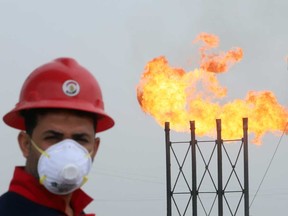 Flames emerge from flare stacks at Nahr Bin Umar oilfield, as a worker wears a protective mask, following an outbreak of coronavirus, north of Basra, Iraq.