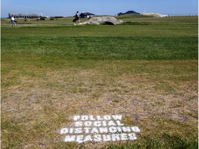A golfer crosses the iconic Swilcan Bridge with a sign on the grass reminding golfers to respect social distancing measures at The Old Course in St Andrews, Scotland on May 29, 2020, as the Scottish Government eases lockdown restrictions during the novel coronavirus COVID-19 pandemic. (Photo by Andy Buchanan / AFP)