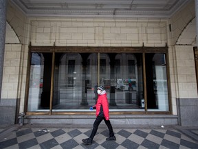 A man wears a mask as he walks past an empty display window at the downtown Calgary Hudson's Bay on Monday, May 11, 2020.