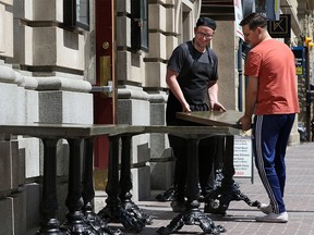 James Joyce Irish Pub staff Connor O'Hare, left and Liam McLaughlan move patio tables out onto Stephen Avenue Mall in downtown Calgary on Wednesday, May 13, 2020.