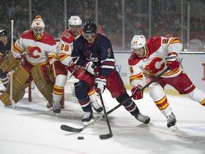 Winnipeg Jets' Dmitry Kulikov and Calgary Flames' Travis Hamonic fight for the puck during the NHL Heritage Classic at Mosaic Stadium in Regina on Oct. 26, 2019. Troy Fleece/Postmedia Network