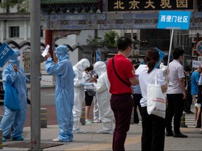 Medical staff in full protective gear carry signs to assist people who live near or who have visited the Xinfadi Market, a wholesale food market where a new COVID-19 coronavirus cluster has emerged, as they arrive for testing in Beijing on June 17, 2020.