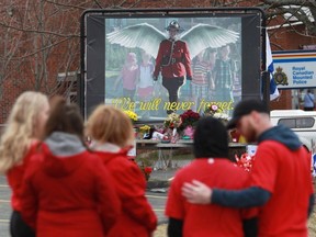 Mourners, asked to wear red on Friday, are seen near a mural dedicated to slain RCMP Const. Heidi Stevenson, during a province-wide, two-minutes of silence for the 22 victims of last weekend's shooting rampage, in front of the RCMP detachment in Cole Harbour, N.S., Friday, April 24, 2020.