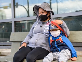 Nanny Cathy Acuerdo, left, and three-year-old Ethan sit on a bench on 12 Ave. S.E. wearing masks on Monday, July 13, 2020.