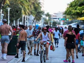In this file photo a man rides a bicycle as people walk on Ocean Drive in Miami Beach, Florida on June 26, 2020.