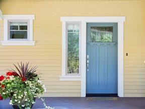 A front entrance of a home with a blue door, yellow siding, and a flowerpot in daytime.