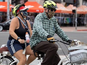 A couple chooses to wear face masks as they ride a tandem bike in Huntington Beach, Calif., July 1, 2020.