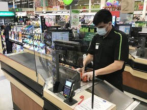 An employee is pictured working behind a Plexiglas shield at a grocery store in North Vancouver on March 22, 2020.