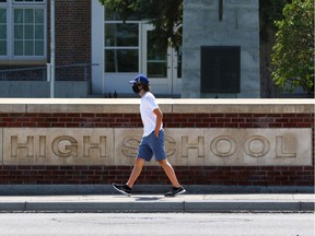 A pedestrian wears a mask as they walk past the Western Canada High School sign in Calgary on Wednesday, July 22, 2020. Some are concerned about the province's decision not to require masks for students returning to school in September. Gavin Young/Postmedia
