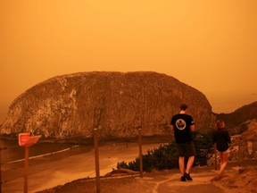 People walk by the Pacific Ocean coast as smoke from wildfires covers an area near Seal Rock, Oregon, Tuesday, Sept. 8, 2020.