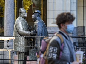 A pedestrian wearing a mask walks in front of the Conversation Sculptures who are too wearing masks on Stephen Avenue on Friday, October 2, 2020.