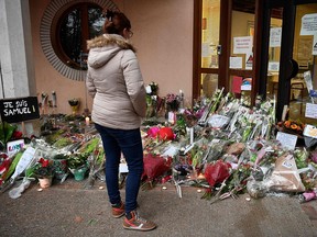A woman looks at flowers at the entrance of a middle school in Conflans-Sainte-Honorine, northwest of Paris, on October 17, 2020, after a teacher was decapitated by an attacker who has been shot dead by policemen.