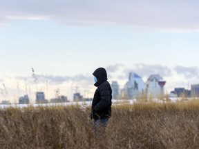 A masked pedestrian walks along the pathway in Valleyview Park with the Calgary skyline under the Chinook arch in the background on Friday, November 20, 2020.
