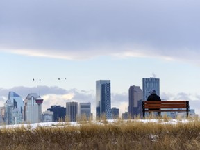 A lone pedestrian sits on a bench in Valleyview Park with the Calgary skyline under the Chinook arch in the background on Friday, November 20, 2020.