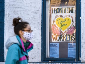 A masked pedestrian walks in front of a sign thanking the frontline workers behind a window in Kensington on Monday, November 23, 2020.