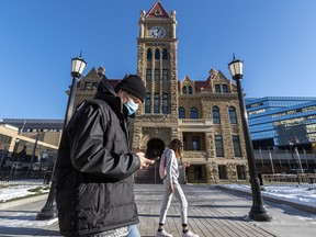Masked pedestrians walk in front of the old city hall in downtown Calgary on Monday, November 23, 2020.