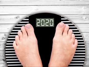2020 feet on a weight scale on white planks, new year and holiday food nutrition and diet concept.