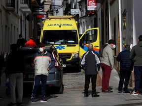 People stand near an ambulance as health-care workers treat a patient suffering from COVID-19 during a home visit in Ronda, southern Spain, Jan. 23, 2021.