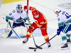 Calgary Flames forward Andrew Mangiapane and Vancouver Canucks defenceman Quinn Hughes battle for the puck in front of Vancouver goaltender Braden Holtby at the Scotiabank Saddledome in Calgary on Jan. 16, 2021.