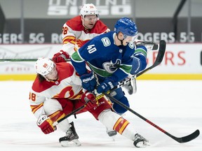 The Calgary Flames’ Andrew Mangiapane (left) and Byron Froese battle the Vancouver Canucks’ Elias Pettersson at Rogers Arena in Vancouver on Monday, Feb. 15.