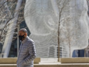 A masked pedestrian takes a walk downtown Calgary with the Wonderland sculpture in the background on Friday, April 16, 2021.