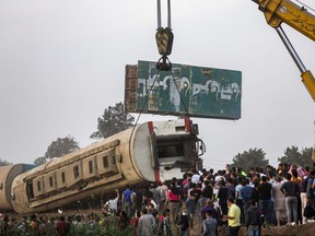 People watch as a telescopic railway crane lifts an overturned passenger carriage at the scene of a railway accident in the city of Toukh in Egypt's central Nile Delta province of Qalyubiya on April 18, 2021.