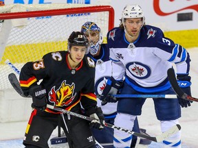 The Calgary Flames’ Johnny Gaudreau and Winnipeg Jets’ Tucker Poolman fight for position in front of Jets goaltender Connor Hellebuyck at the Saddledome in Calgary on Friday, March 26, 2021.