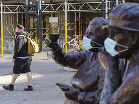 A pedestrian walks by the Famous Five, who have been adorned with masks in Calgary on Friday, April 16, 2021.
