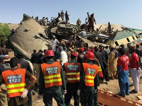 Rescue workers stand as people gather at the site following a collision between two trains in Ghotki, Pakistan June 7, 2021.