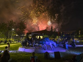 People relax in the evening warmth around the By the Banks of the Bow bronzes to watch the fireworks show at the Calgary Stampede on Tuesday, July 13, 2021.