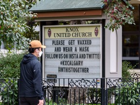 A masked pedestrian walks in front of a sign outside Knox United Church in downtown Calgary encouraging people to get vaccinated and wear mask to help prevent the spread of COVID-19 on Friday, September 17, 2021. Azin Ghaffari/Postmedia